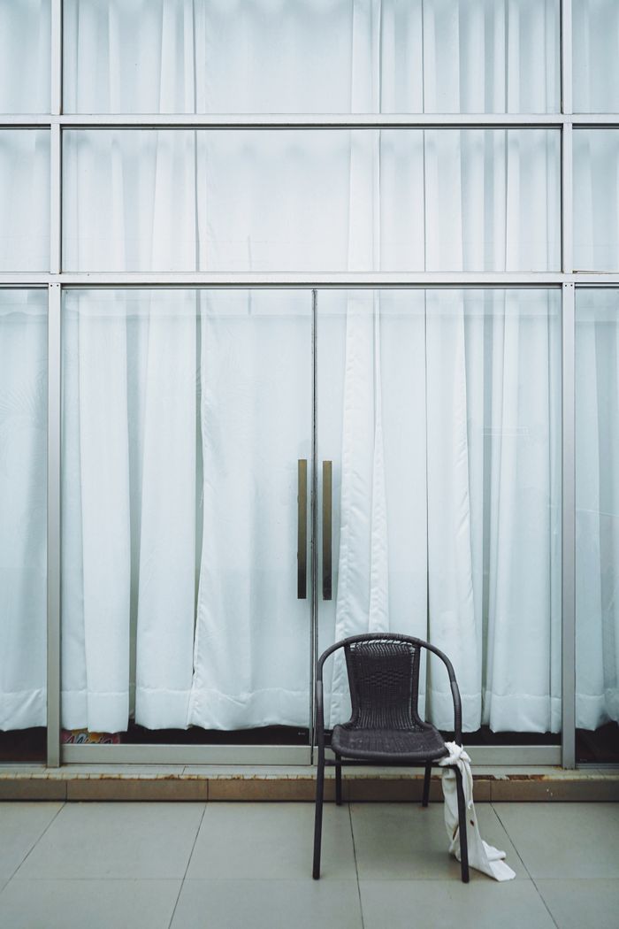 gallery-02 Simple interior scene with a chair in front of large glass doors and white curtains.
