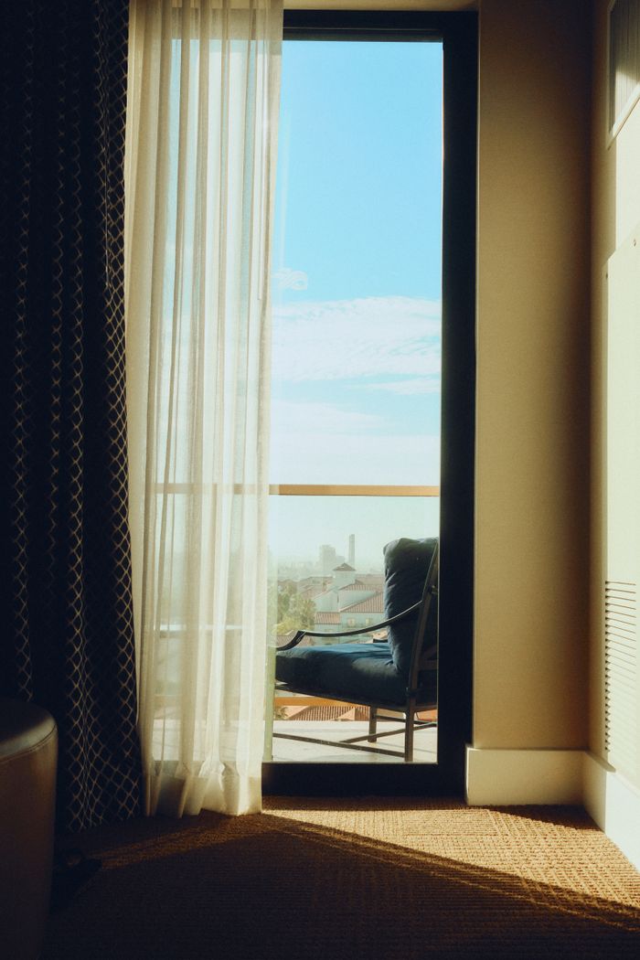 gallery-03 A serene hotel room with elegant sheer curtains opening to a sunlit balcony view.