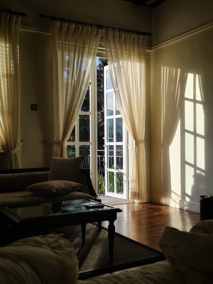 Home A warm and inviting living room with sunlight streaming through open French doors, casting soft shadows.